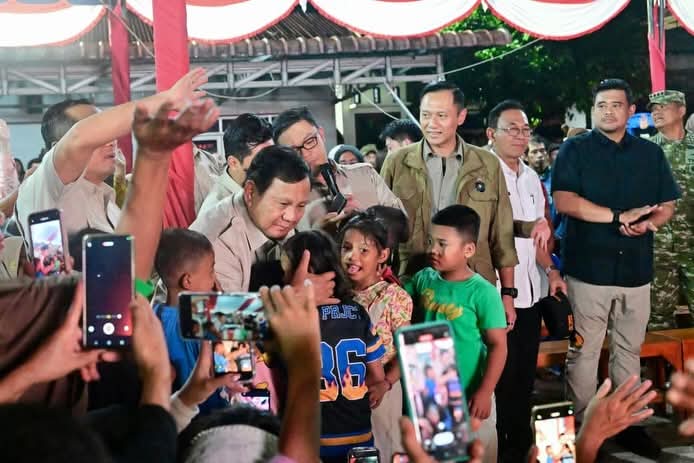 President Prabowo Subianto engages with local children during a high-stakes coordination meeting in Aceh Tamiang (01/01/2026). By deploying a "full-cabinet convoy" including 10 ministers and 15 SOE CEOs, the administration demonstrates that a massive state-led mobilization can deliver "all-out" disaster recovery without the legal escalation of a national emergency status. (BPMI Setpres/GETNEWS+)